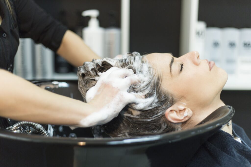 Hair stylist or barber exhibiting good hair salon safety in a slip fall hazard scenario, where she’s washing a client’s hair.