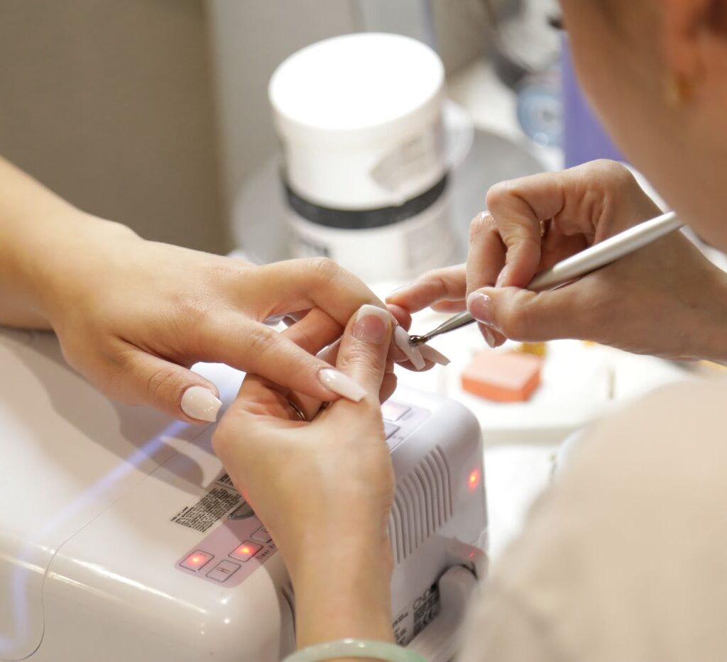 Nail salon technician practices manicure health and safety with a client’s nails.