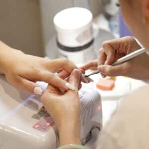 Nail salon technician practices manicure health and safety with a client’s nails.