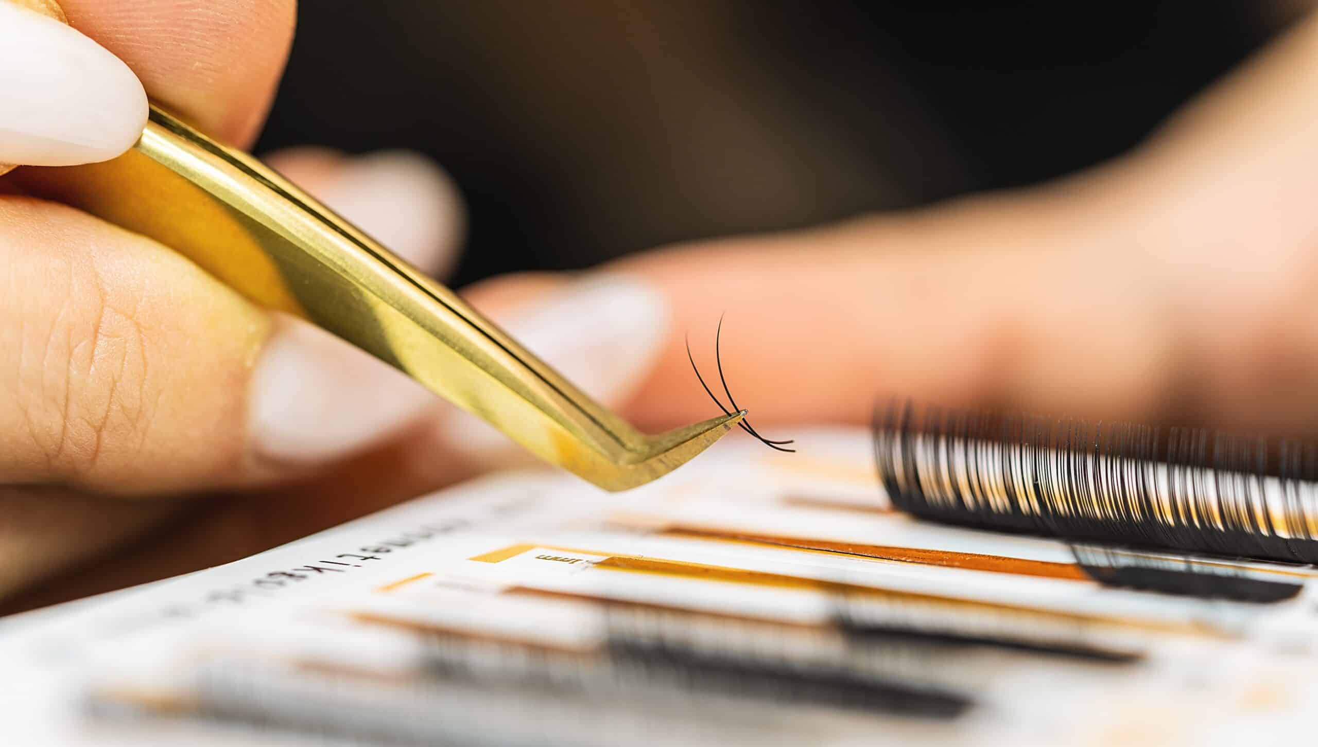 Close up of a cosmetologist or other beauty specialist using tweezers to select eyelash extensions. Clean tools can prevent some eyelash extensions gone wrong horror stories.