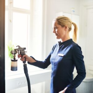 Female spray tan specialist wearing a blue uniform and using a spray bottle on a female client. Specialists like this should follow spray tan tips like standing farther away from clients.