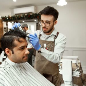 Male barber wears blue PPE hairdressing gloves as he cuts hair to avoid contact dermatitis hairdressing