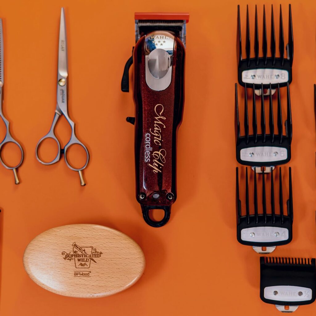 Orange background featuring an array of barber tools and equipment, such as clippers, spare blades, shears, trimmers, and a brush. The tools are neat and organized, showing proper hair clippers maintenance, how to clean barber clippers, and how to sterilize hair clippers and other tools.