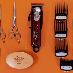 Orange background featuring an array of barber tools and equipment, such as clippers, spare blades, shears, trimmers, and a brush. The tools are neat and organized, showing proper hair clippers maintenance, how to clean barber clippers, and how to sterilize hair clippers and other tools.