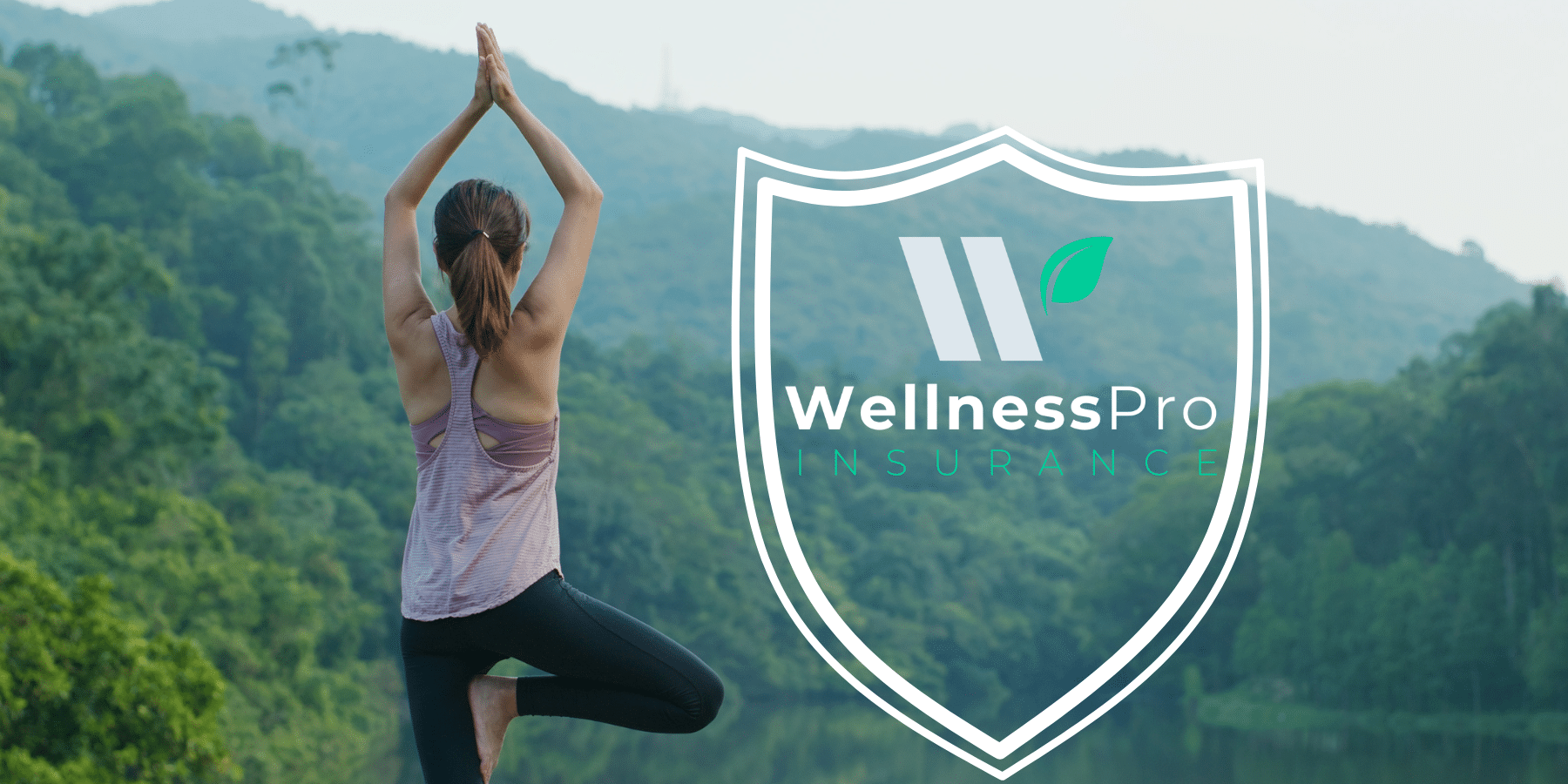 Woman stands in a balancing yoga tree pose facing away from the camera toward mountains and lush, green trees. She stands tall and confident, like someone backed by professional beauty, fitness, and wellness liability insurance for your business.