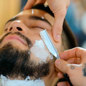 Close-up of a man’s face while receiving a barber straight razor shave around his beard.