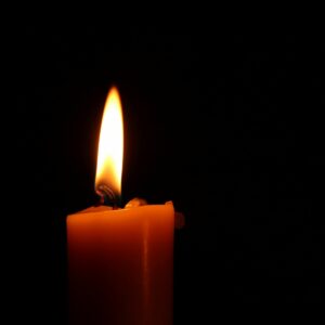 A single candle lit against a black background, illustrating fire hazards in a salon. Putting out candles before you leave is important for fire safety in a salon.