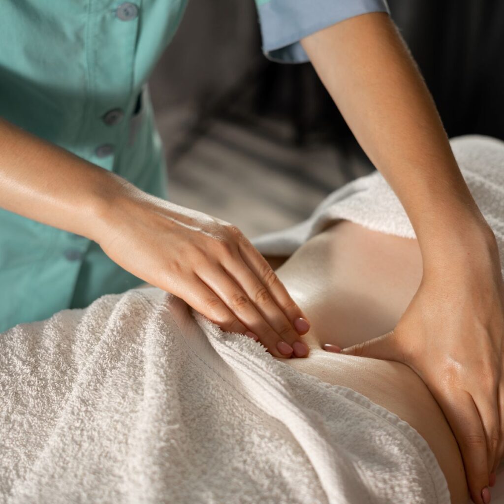 Massage therapist wearing scrubs performs a lymphatic system drainage massage on a client who’s covered with towels.