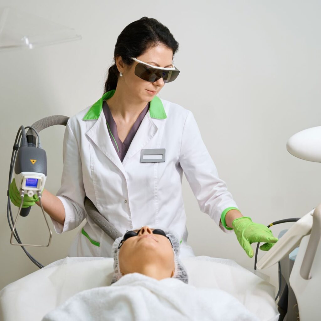 While working as an esthetician, a woman wearing safety goggles, protective gloves, and a lab coat demonstrates a safe esthetician work environment while performing a laser procedure on a client.