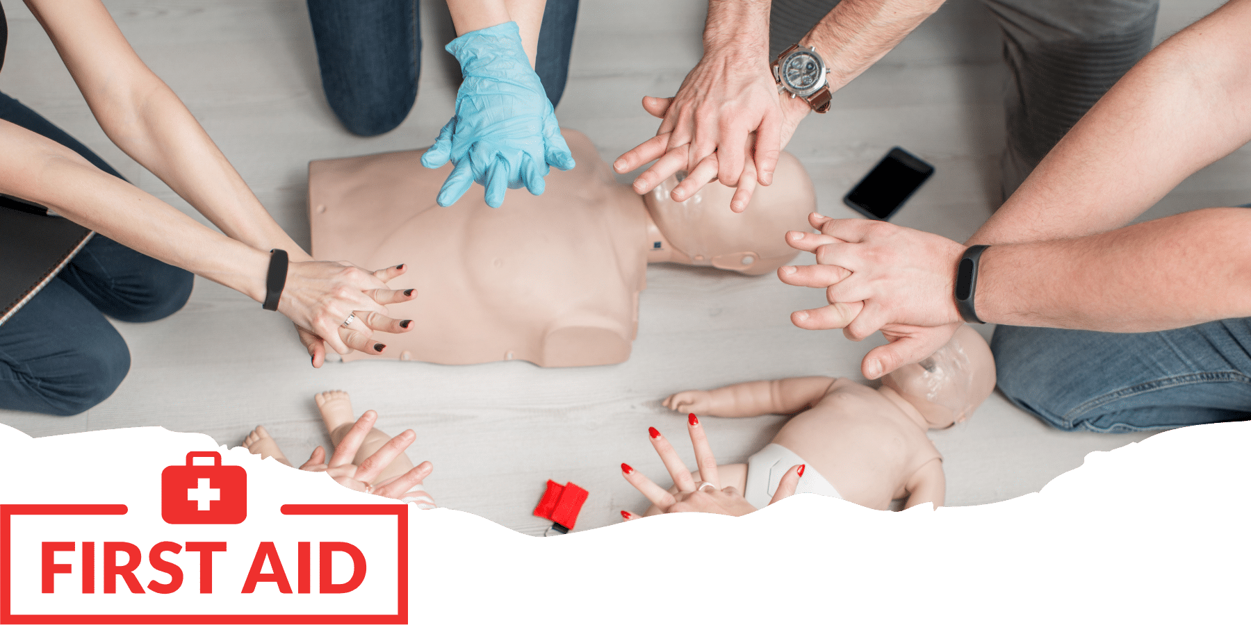 People train to perform CPR on first aid training dummies, with a workplace first aid kit and supplies
nearby.