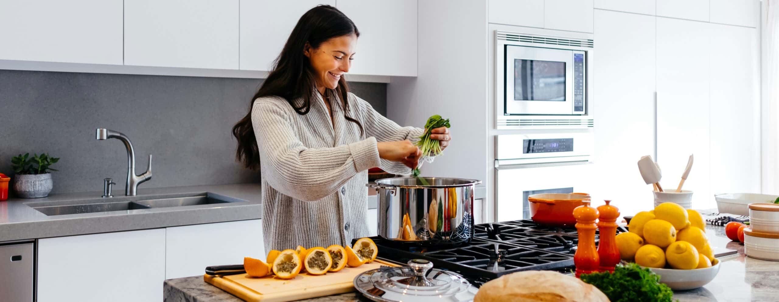 Person in kitchen adding herbs and vegetables to a cooking pot, perhaps acting on advice from a nutritionist.