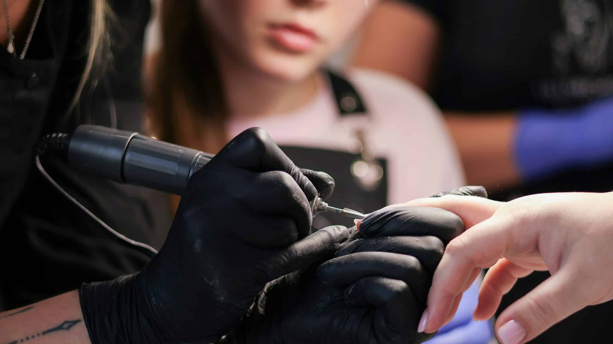 Two women nail technicians using a filing tool to work on a client's gel nail enhancements.