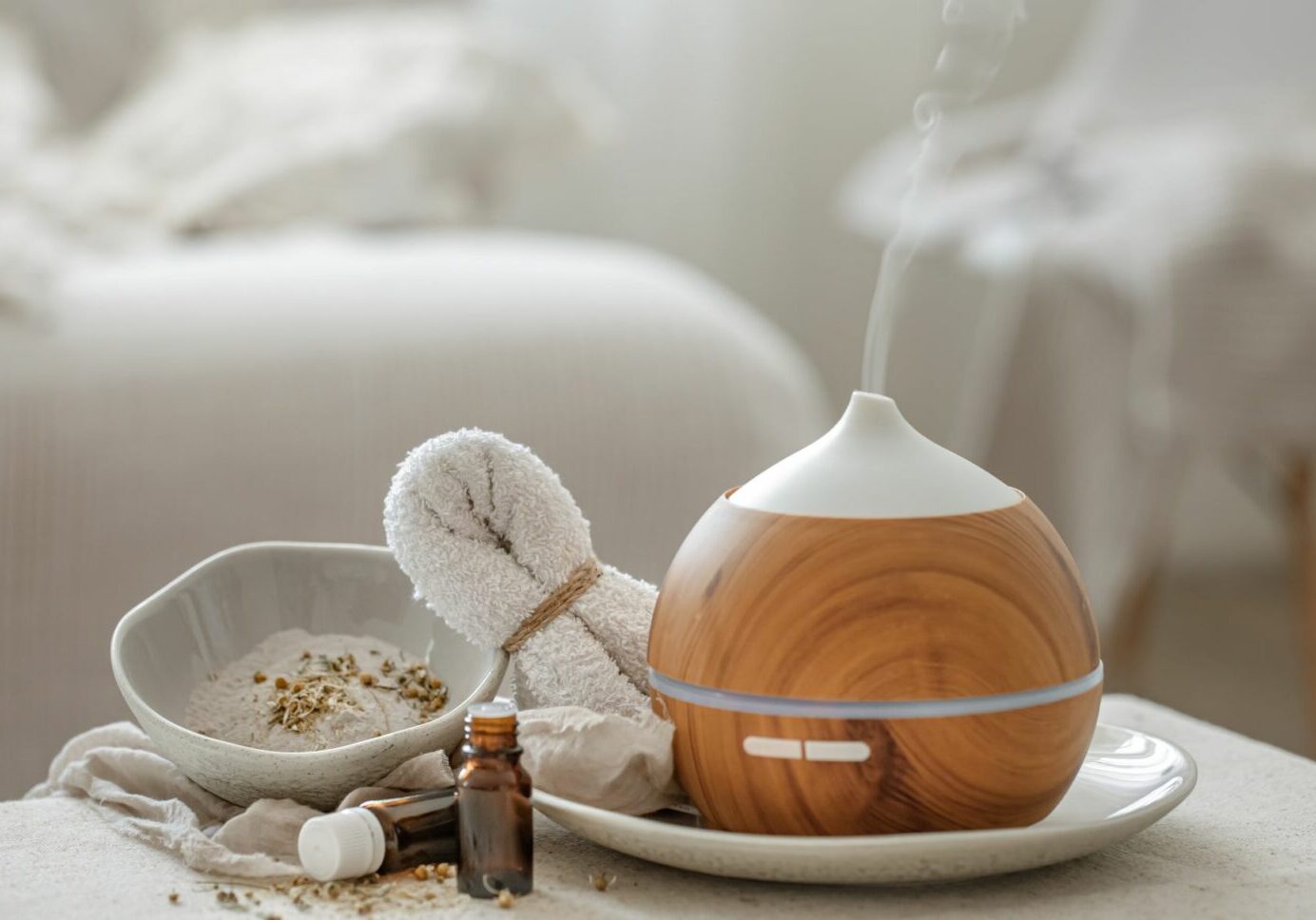 Essential oil diffuser displayed in a wellness spa next to bottles of essential oils, a bowl of dried plants, and a washcloth. Massage aromatherapy services like this one should address health claims regarding essential oils to prevent accidents.