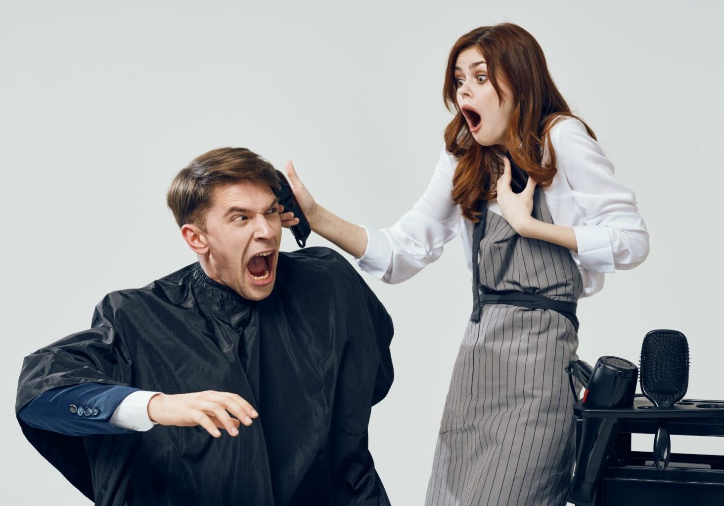 Man in a barbershop or salon chair with a shocked expression while his barber or hairstylist seems to accidentally cut him with clippers. A bad cut could lead to a hair salon lawsuit or barber problem.