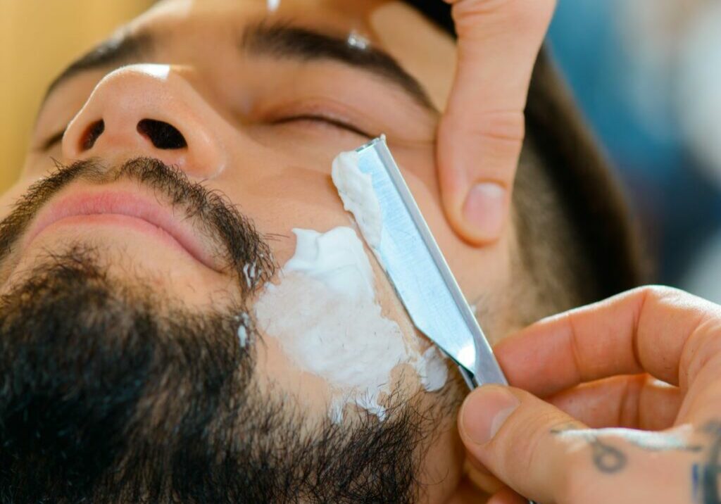 Close-up of a man’s face while receiving a barber straight razor shave around his beard.