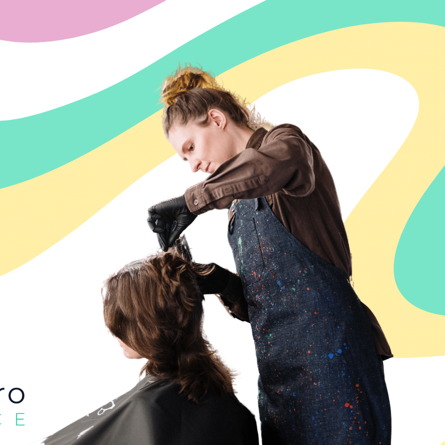 Hairdresser or barber, who likely has cosmetologist insurance, wearing a paint-splattered apron puts product in client’s hair. Featuring WellnessPro Insurance logo and swirly background of pink, yellow, and green.