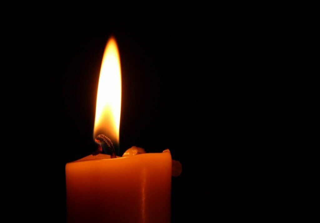 A single candle lit against a black background, illustrating fire hazards in a salon. Putting out candles before you leave is important for fire safety in a salon.