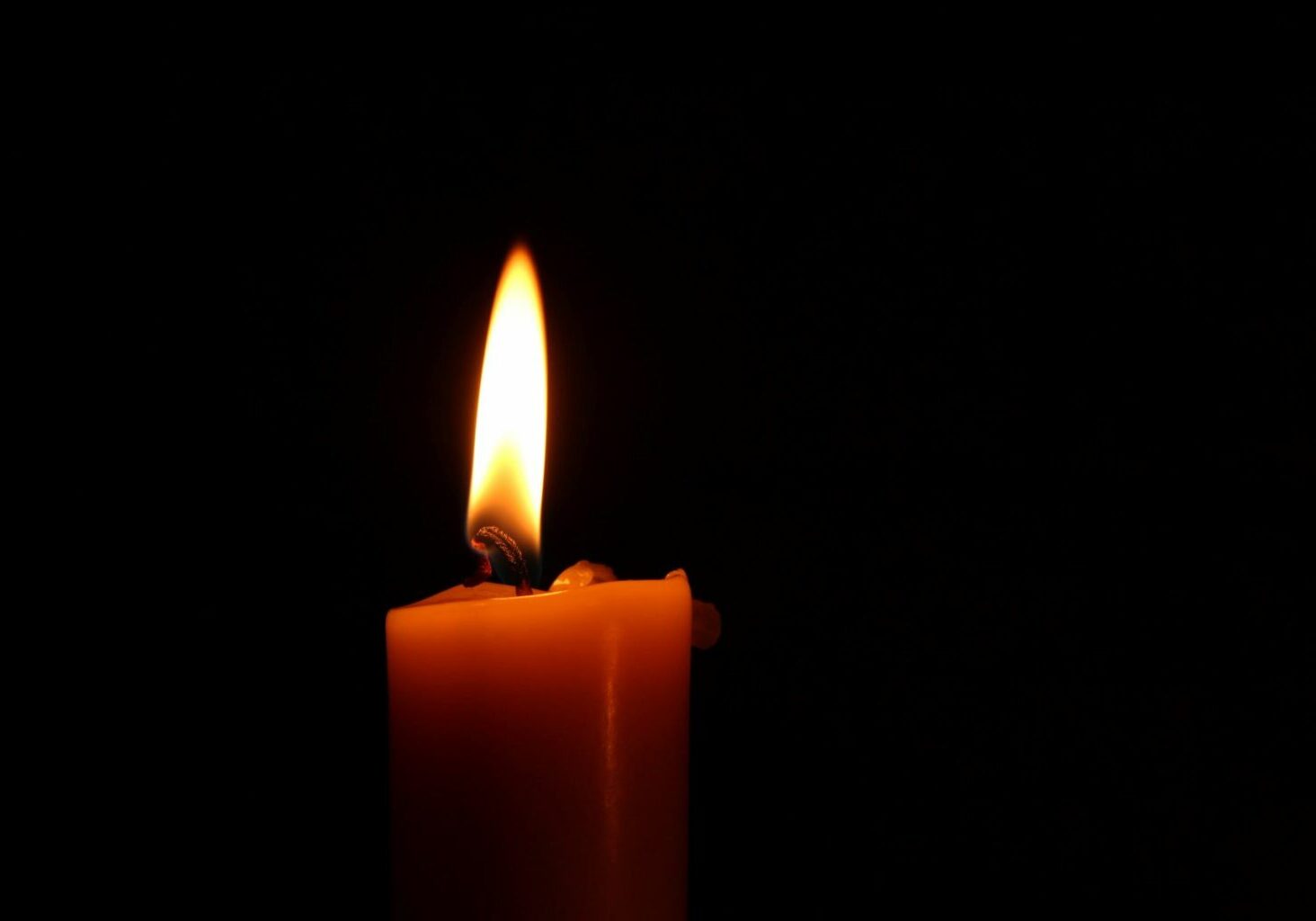 A single candle lit against a black background, illustrating fire hazards in a salon. Putting out candles before you leave is important for fire safety in a salon.