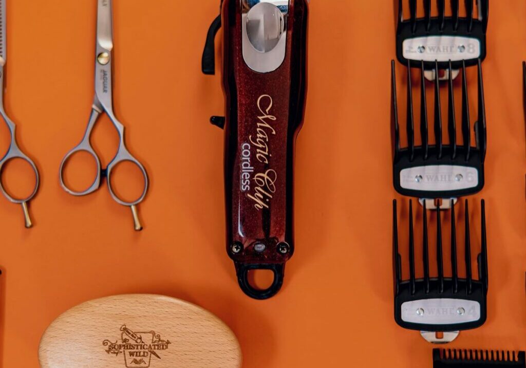 Orange background featuring an array of barber tools and equipment, such as clippers, spare blades, shears, trimmers, and a brush. The tools are neat and organized, showing proper hair clippers maintenance, how to clean barber clippers, and how to sterilize hair clippers and other tools.