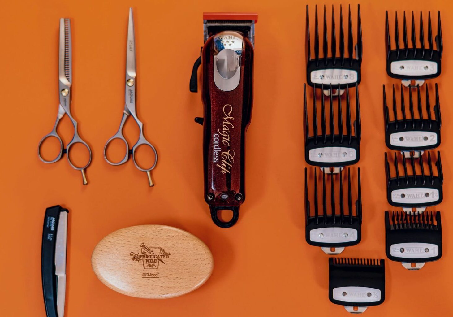 Orange background featuring an array of barber tools and equipment, such as clippers, spare blades, shears, trimmers, and a brush. The tools are neat and organized, showing proper hair clippers maintenance, how to clean barber clippers, and how to sterilize hair clippers and other tools.