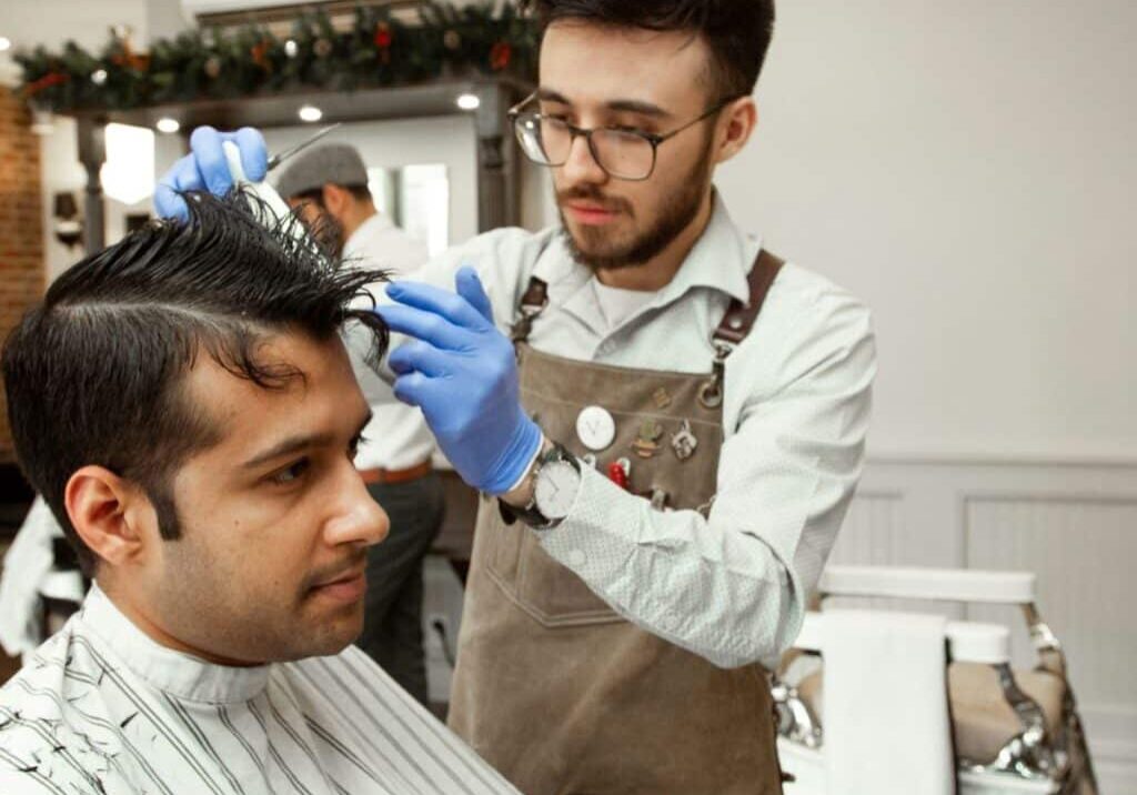 Male barber wears blue PPE hairdressing gloves as he cuts hair to avoid contact dermatitis hairdressing