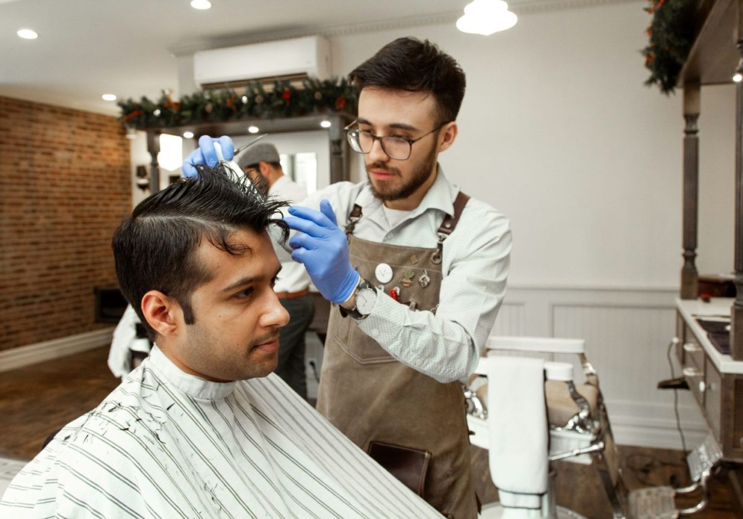 Male barber wears blue PPE hairdressing gloves as he cuts hair to avoid contact dermatitis hairdressing