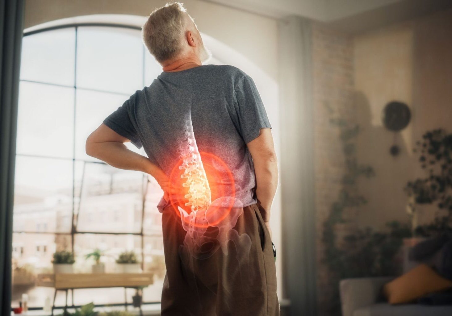 Man standing in an apartment holding his lower back in pain, with a circle around his lower spine indicating inflammation and discomfort after an injury from massage.