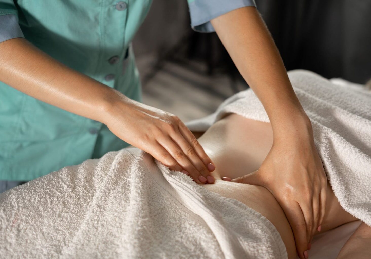 Massage therapist wearing scrubs performs a lymphatic system drainage massage on a client who’s covered with towels.