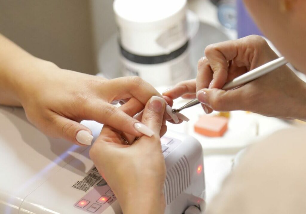 Nail salon technician practices manicure health and safety with a client’s nails.