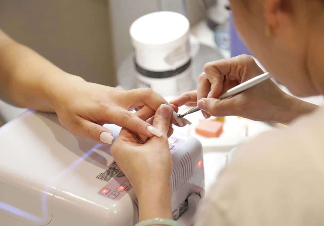 Nail salon technician practices manicure health and safety with a client’s nails.