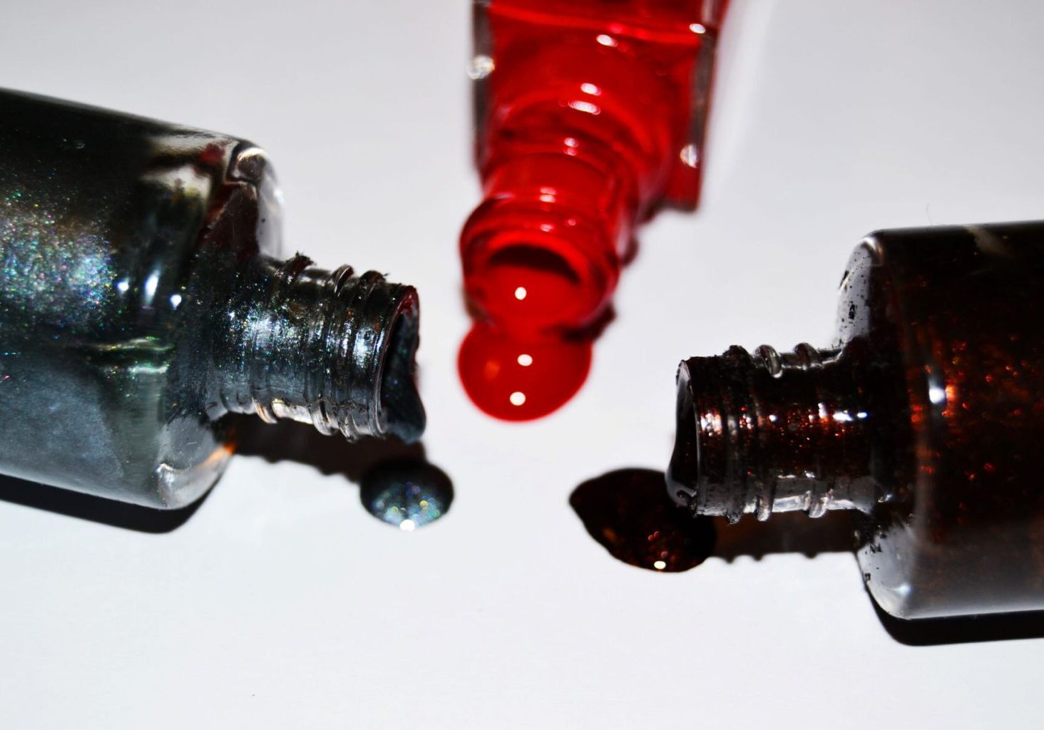 Three bottles of dark-colored nail polish tipped over and spilled onto a white surface, alluding to hazardous chemicals found in nail salon products and ingredients in nail polish.