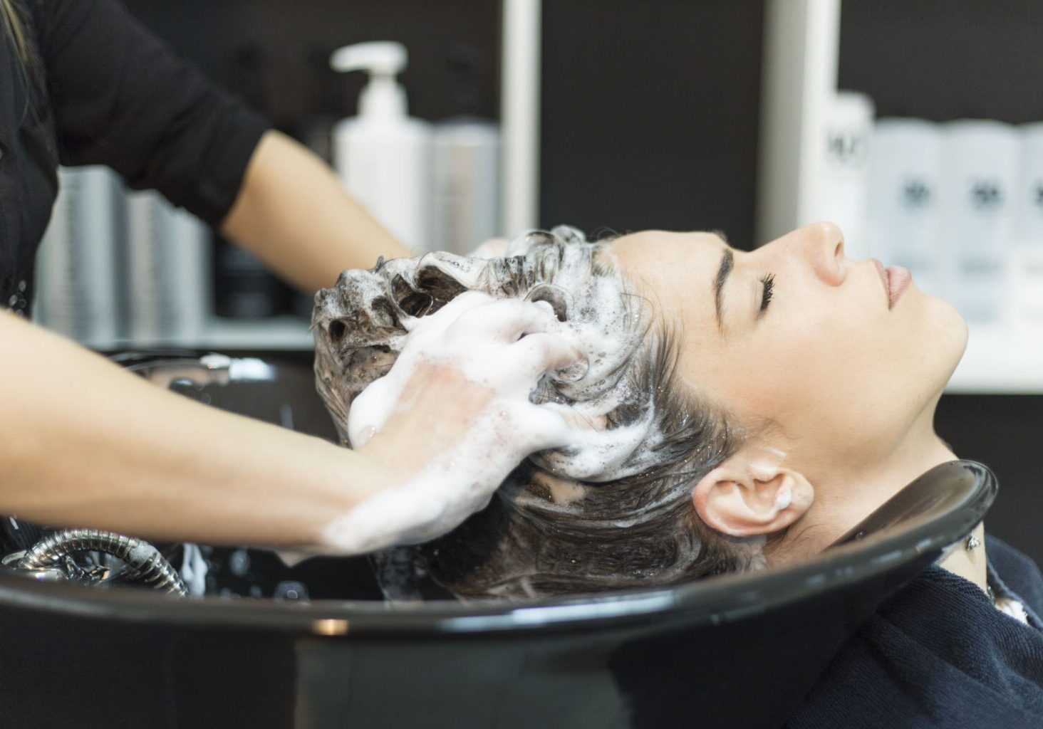 Hair stylist or barber exhibiting good hair salon safety in a slip fall hazard scenario, where she’s washing a client’s hair.