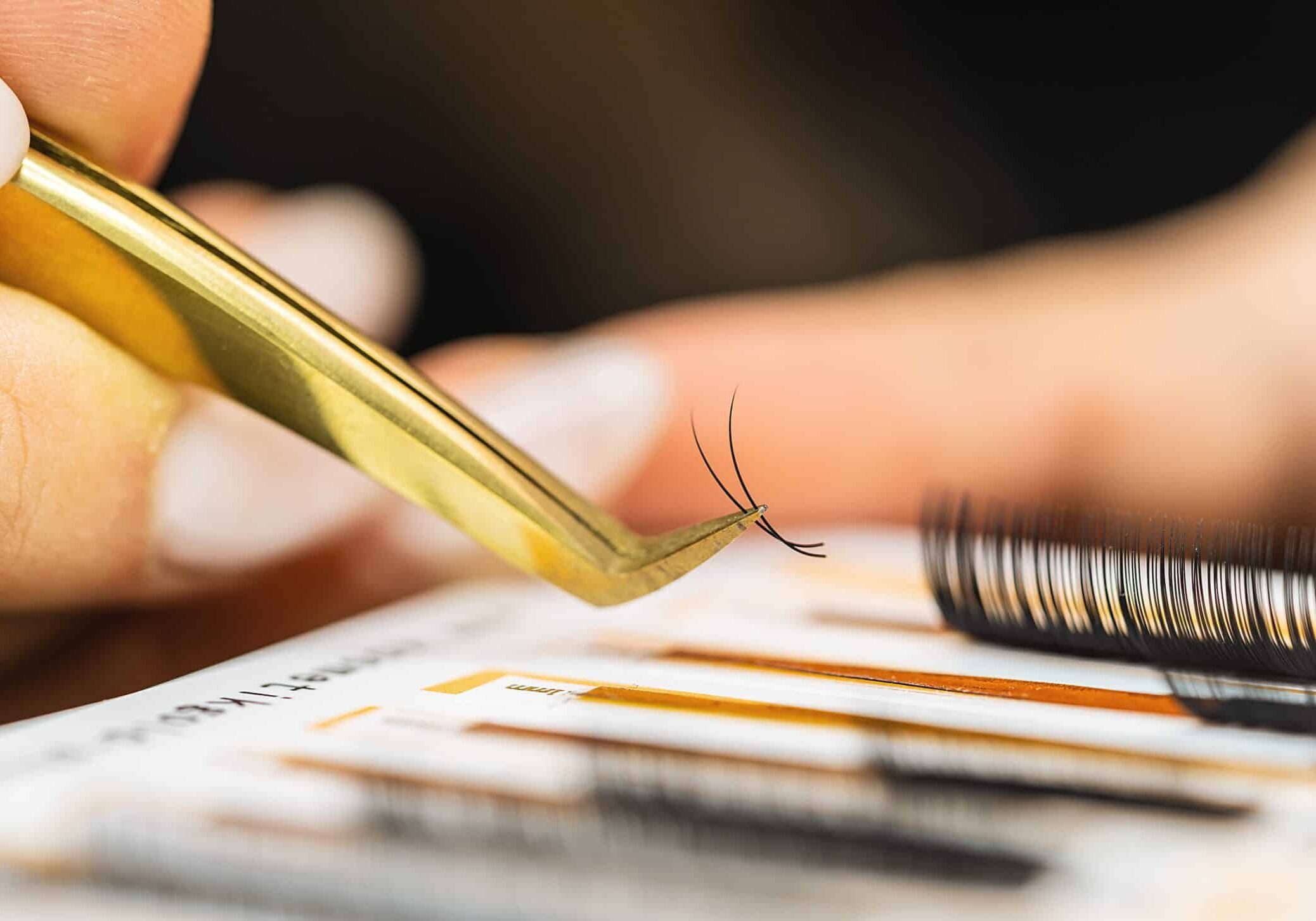 Close up of a cosmetologist or other beauty specialist using tweezers to select eyelash extensions. Clean tools can prevent some eyelash extensions gone wrong horror stories.